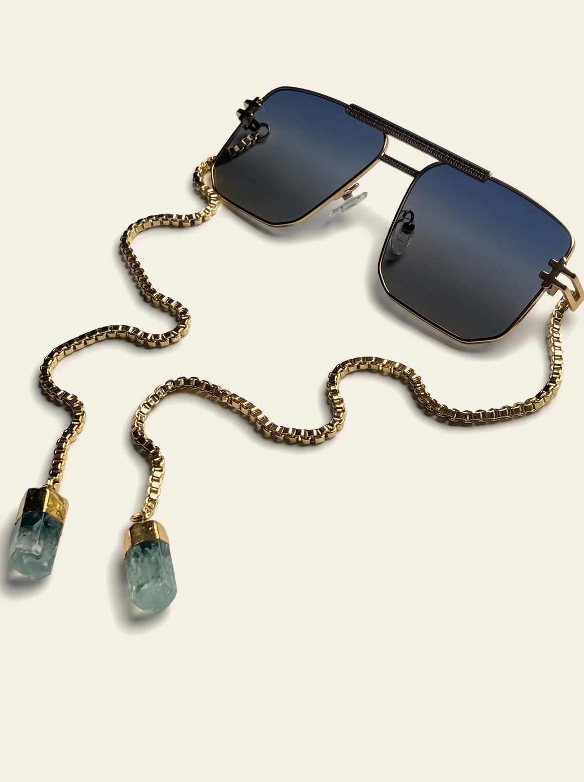 The Portofino - VANNAE temple-less navigator sunglasses with blue-grey lenses and a gold chain finished with two green quartz stones, three-quarter view