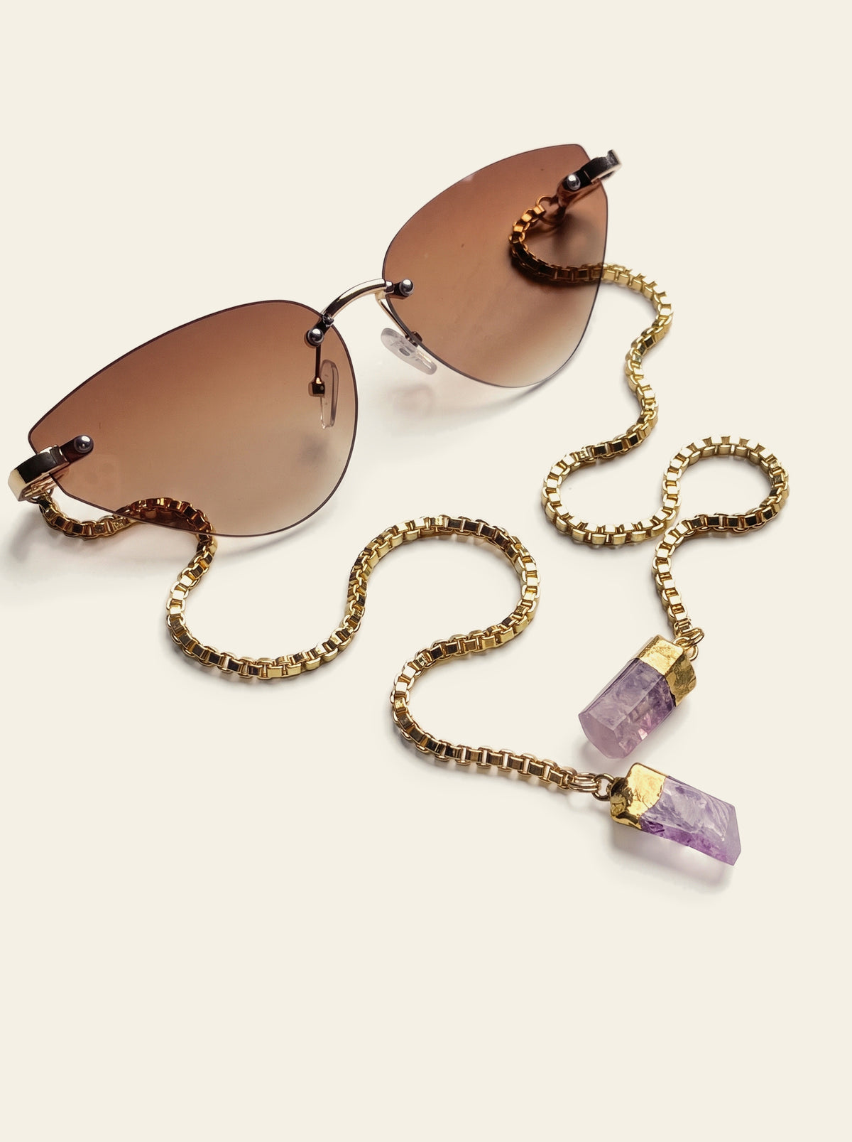 The Capri - top view of rimless cat-eye sunglasses with brown gradient lenses and a slim gold bridge, gold chain trailing forward