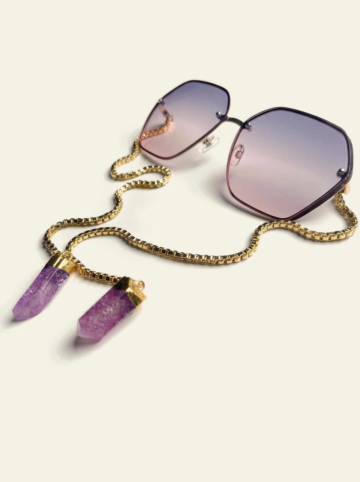 The Positano - rimless hexagon sunglasses with grey-pink gradient lenses, three-quarter view, gold chain trailing to two purple quartz stones