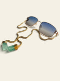 The Ravello - thin gold square frame sunglasses with blue-grey gradient lenses and a gold box chain ending in two raw green quartz stones, three-quarter view