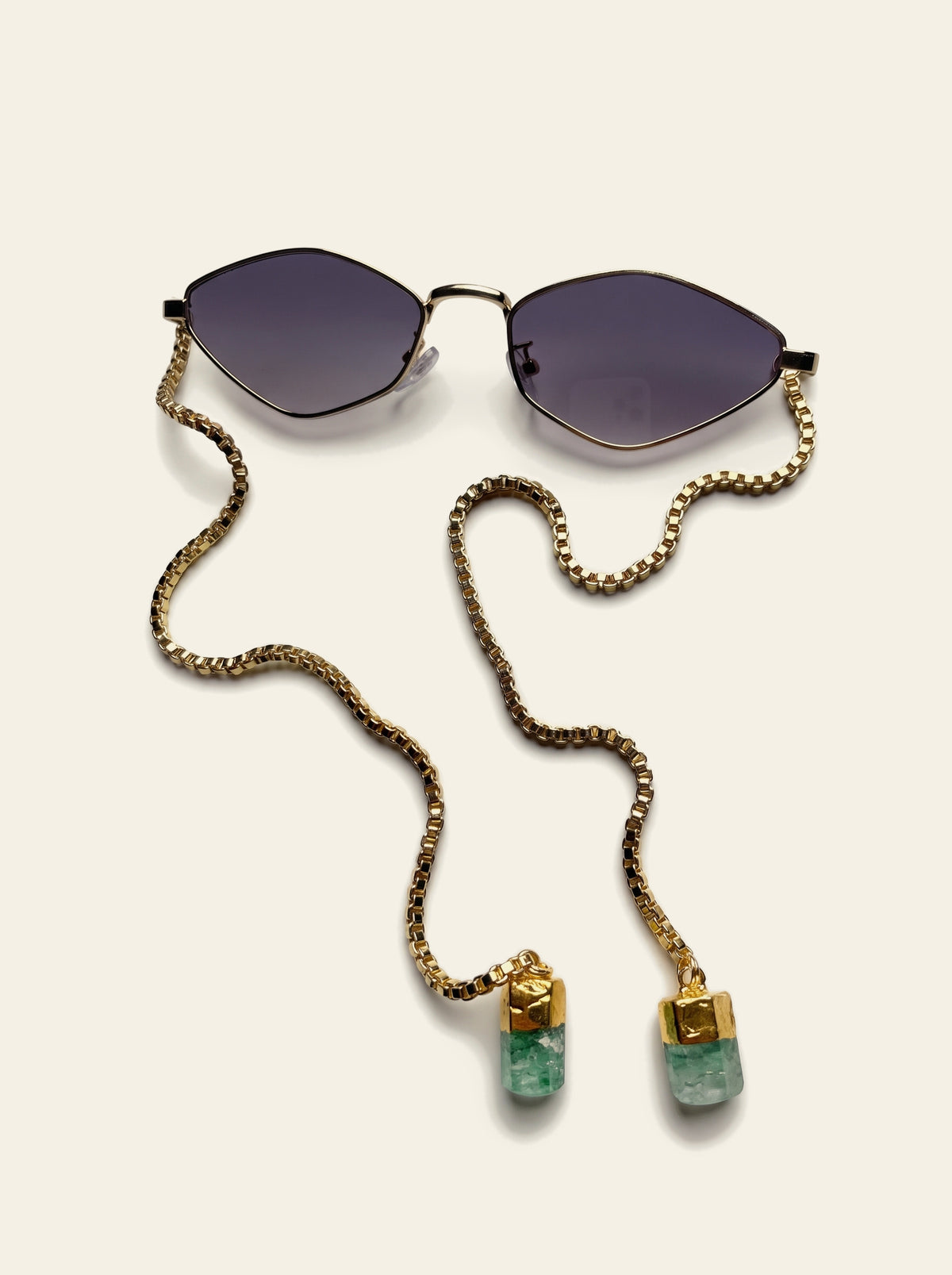 The Sorrento - top view of the thin gold diamond frame with purple-grey gradient lenses, gold box chain draped to two raw green quartz stones
