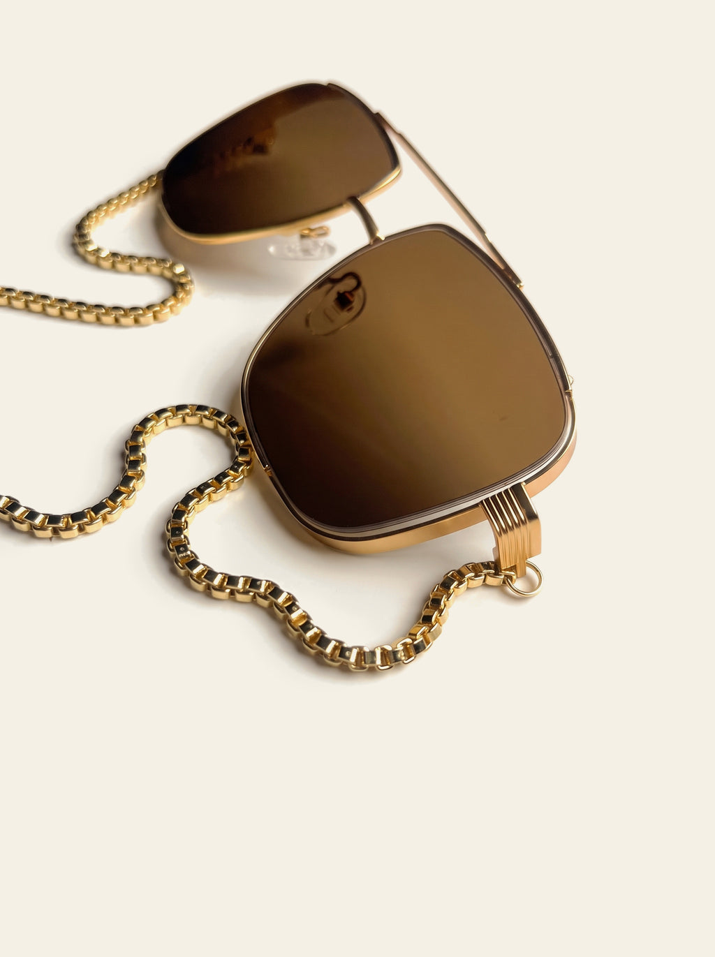 The Como - close-up of warm brown lens and gold double bridge with the gold box chain coiled beside the frame