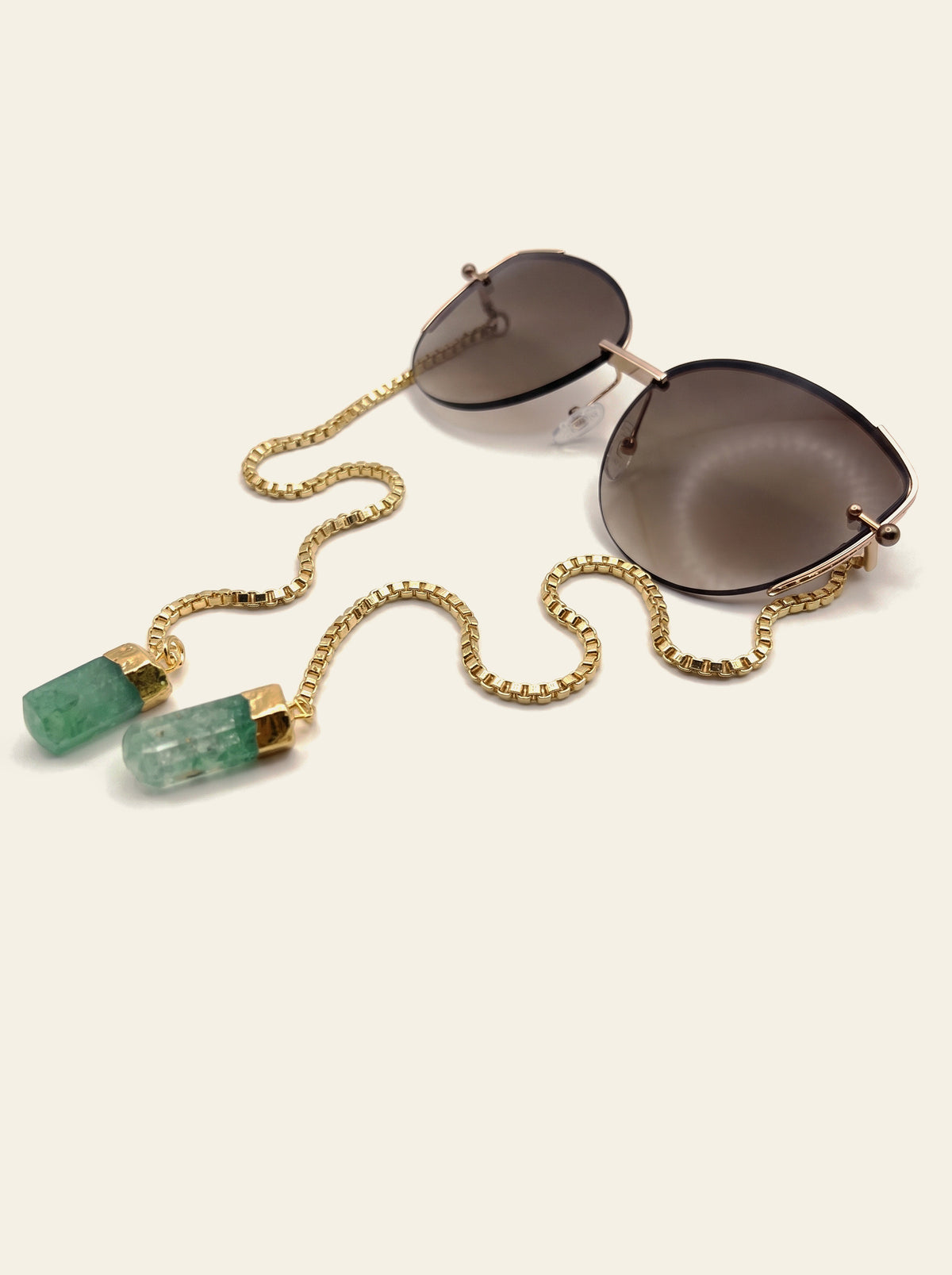 The Cannes - gold semi-rimless butterfly sunglasses with brown gradient lenses, three-quarter view with gold chain and two raw green quartz stones