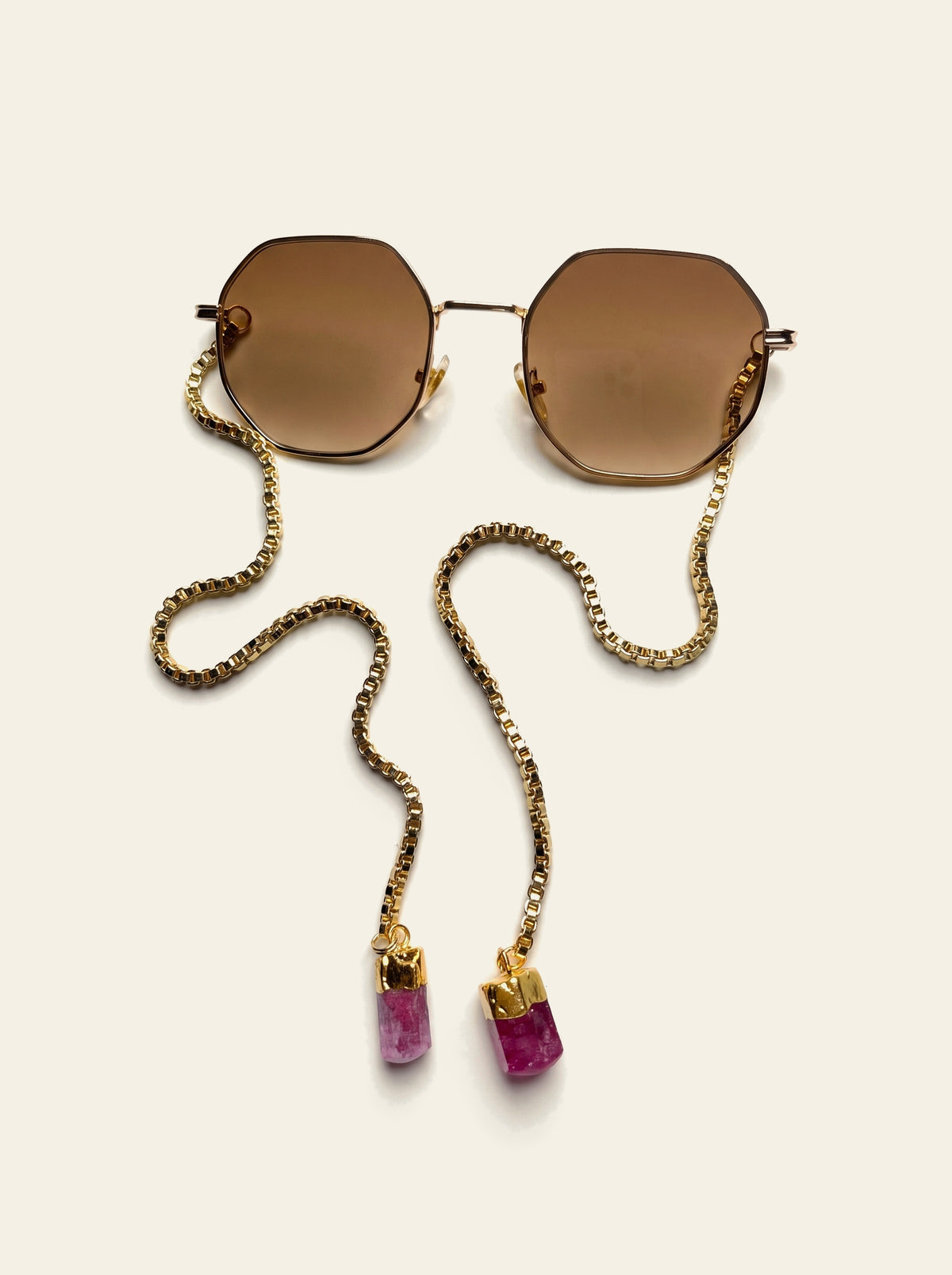 The Sanremo - gold octagon frame with brown lenses laid flat, 18K gold-plated box chain draped to two pink quartz stones, top view