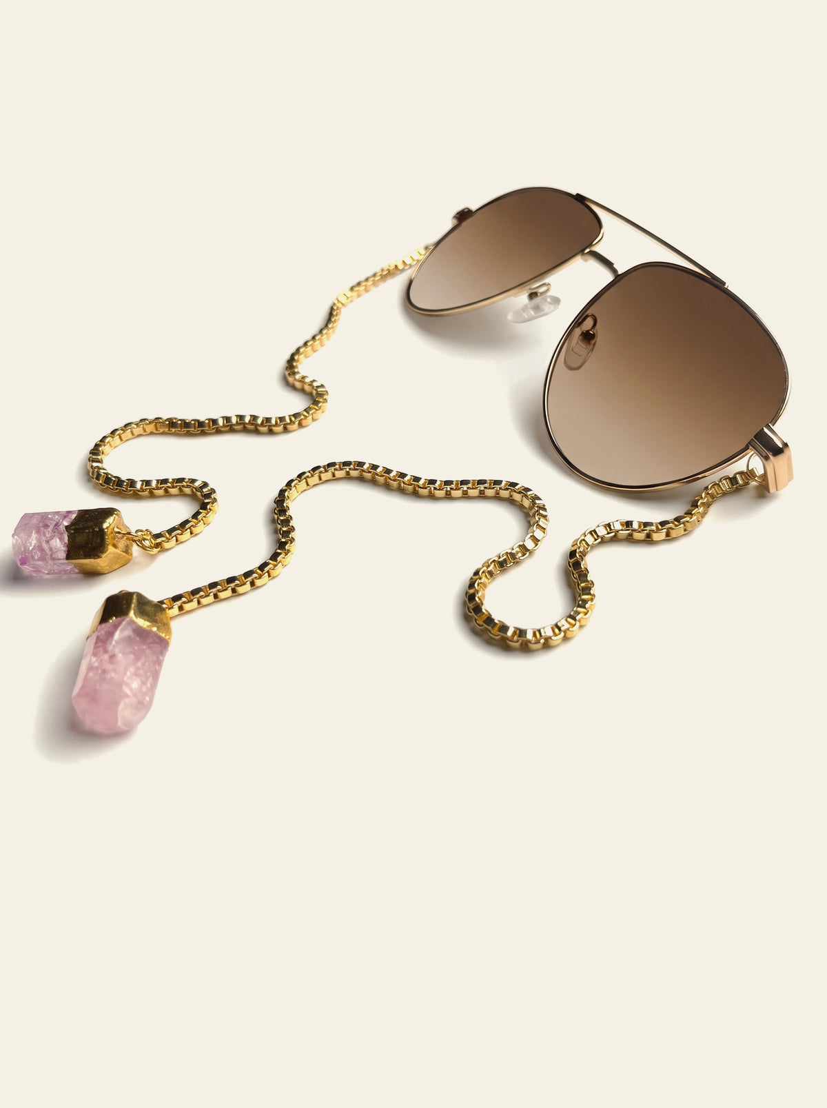 The Monaco - gold aviator sunglasses with brown gradient lenses, three-quarter view, gold box chain draped to two raw pink quartz stones
