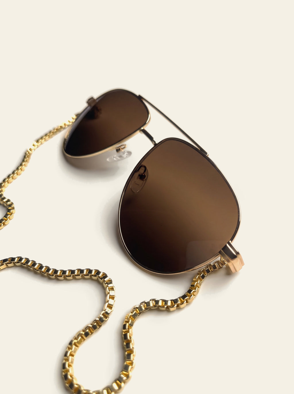 The Monaco - front view of the gold aviator with brown lenses, gold chain hanging below to two pink quartz stones