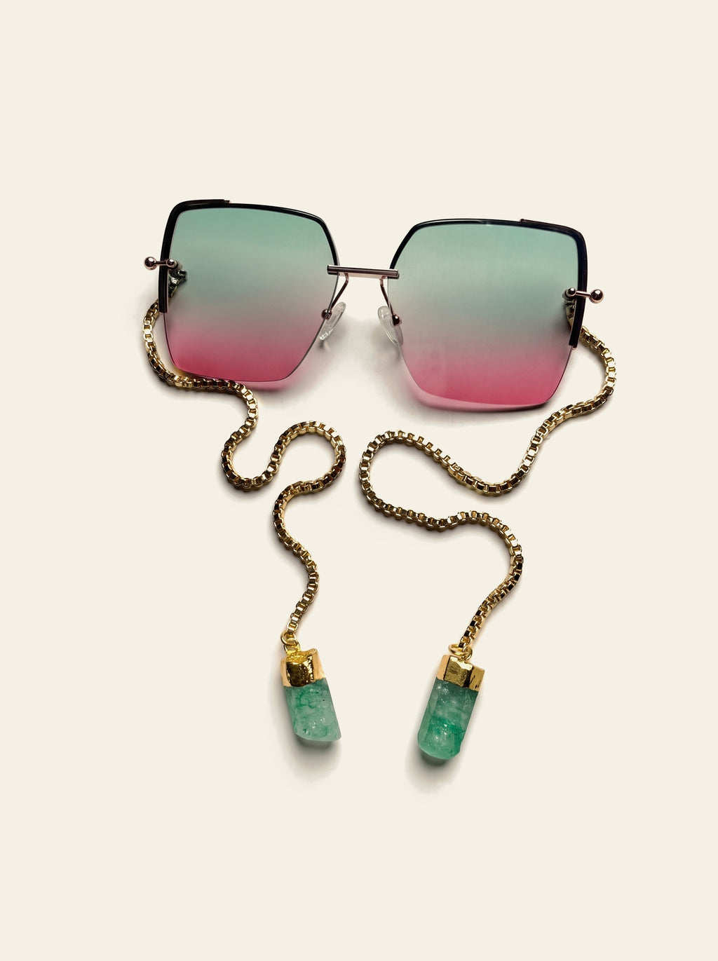 The Marbella - top view of oversized rimless square gold frame with green-to-pink gradient lenses and gold box chain ending in two raw green quartz stones
