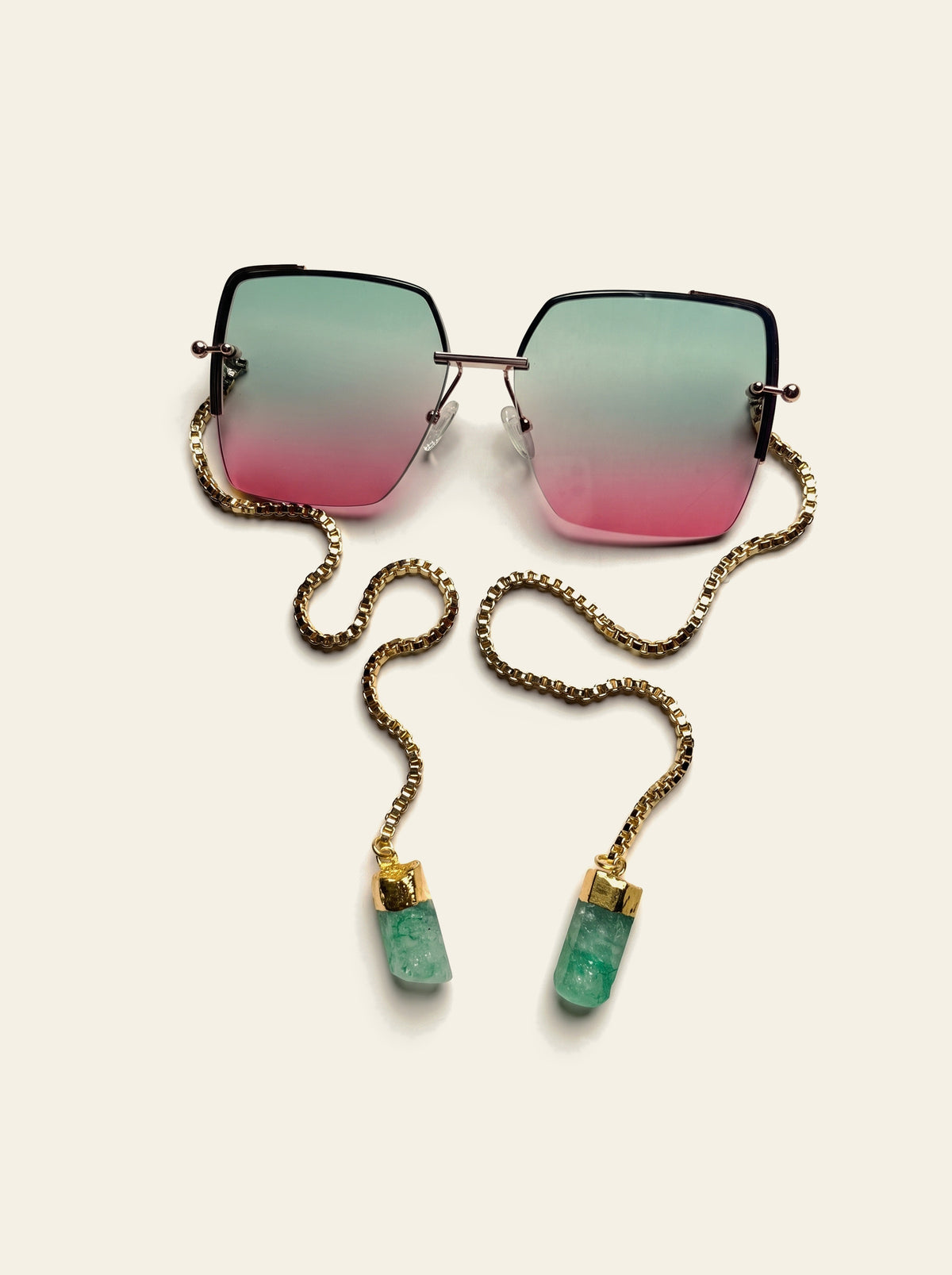The Marbella - top view of oversized rimless square gold frame with green-to-pink gradient lenses and gold box chain ending in two raw green quartz stones