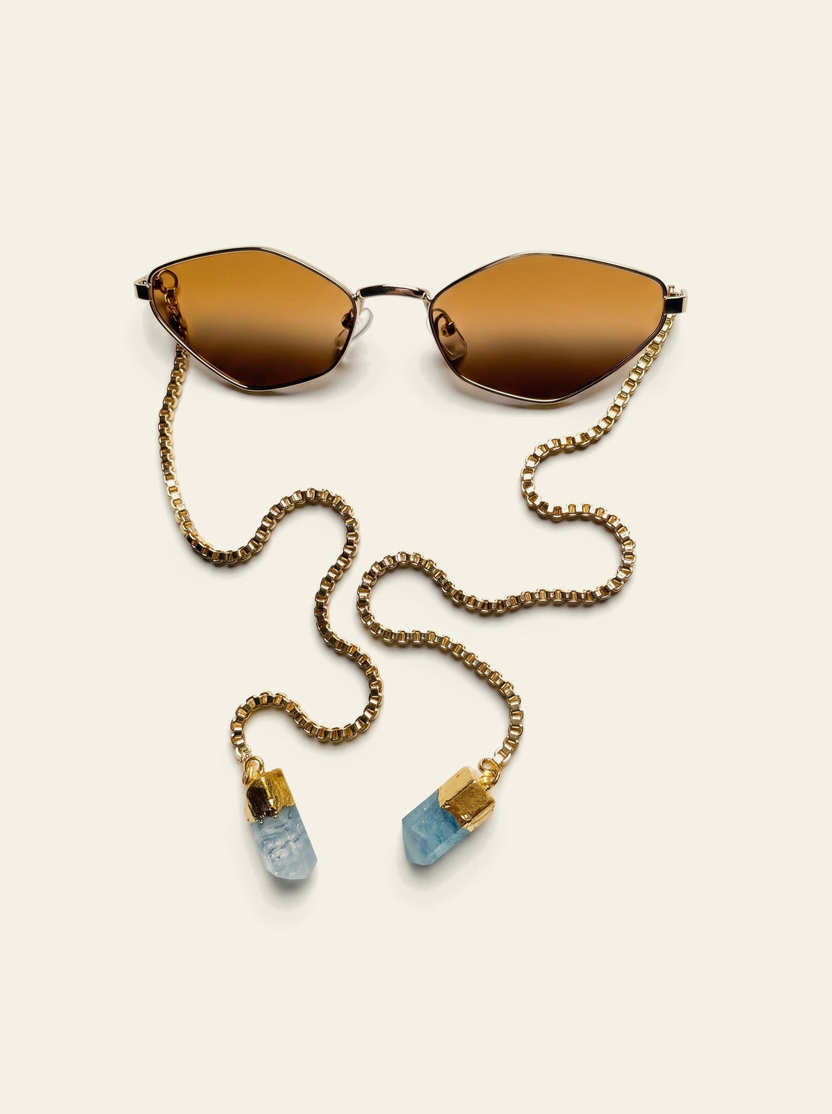The Cassis - top view of thin gold hexagon frame with warm brown lenses, gold box chain and blue quartz stones laid out