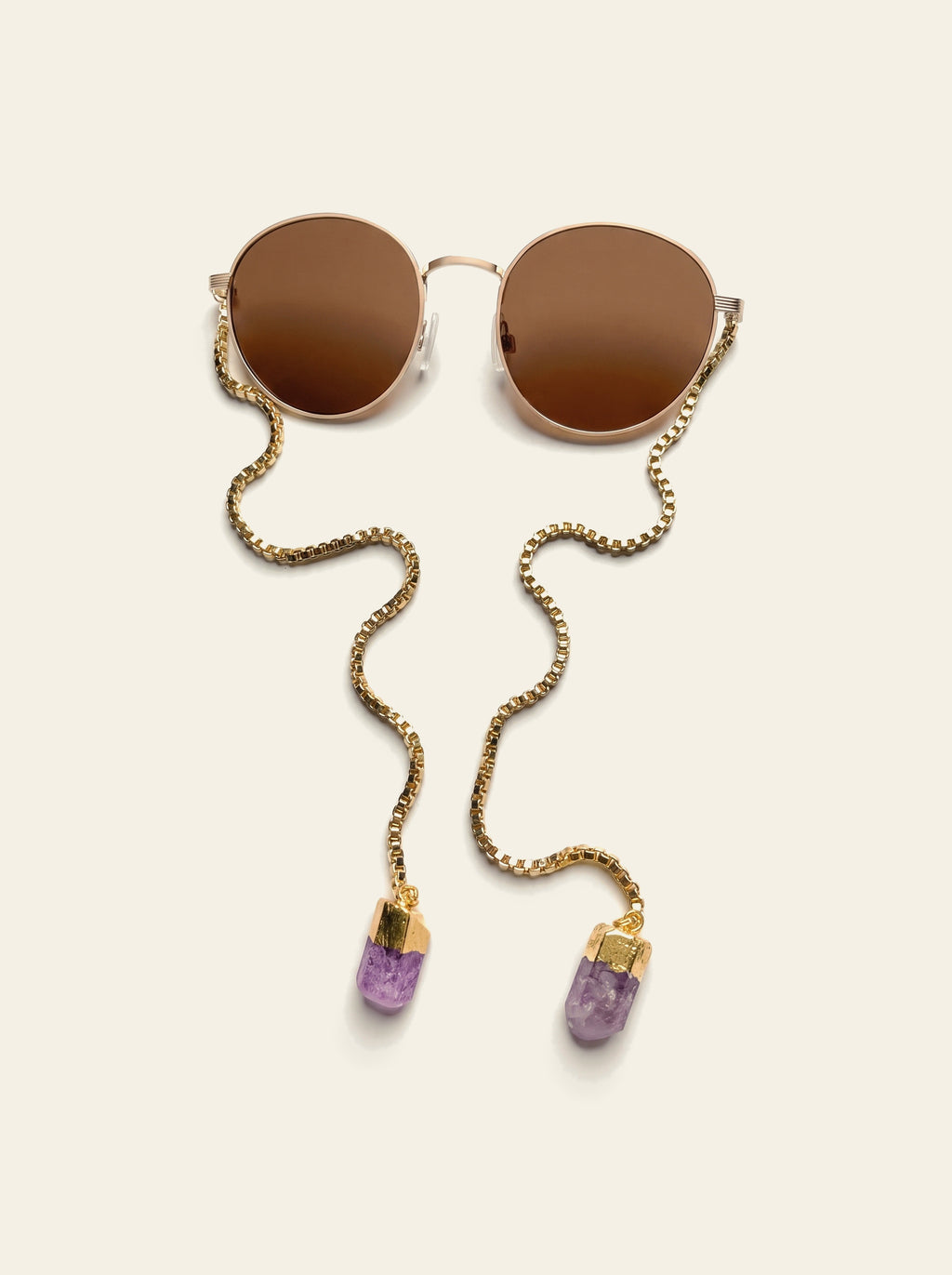 The Procida - top view of round gold frame with brown lenses, the temple-less gold chain draping down to two purple quartz stones in gold caps