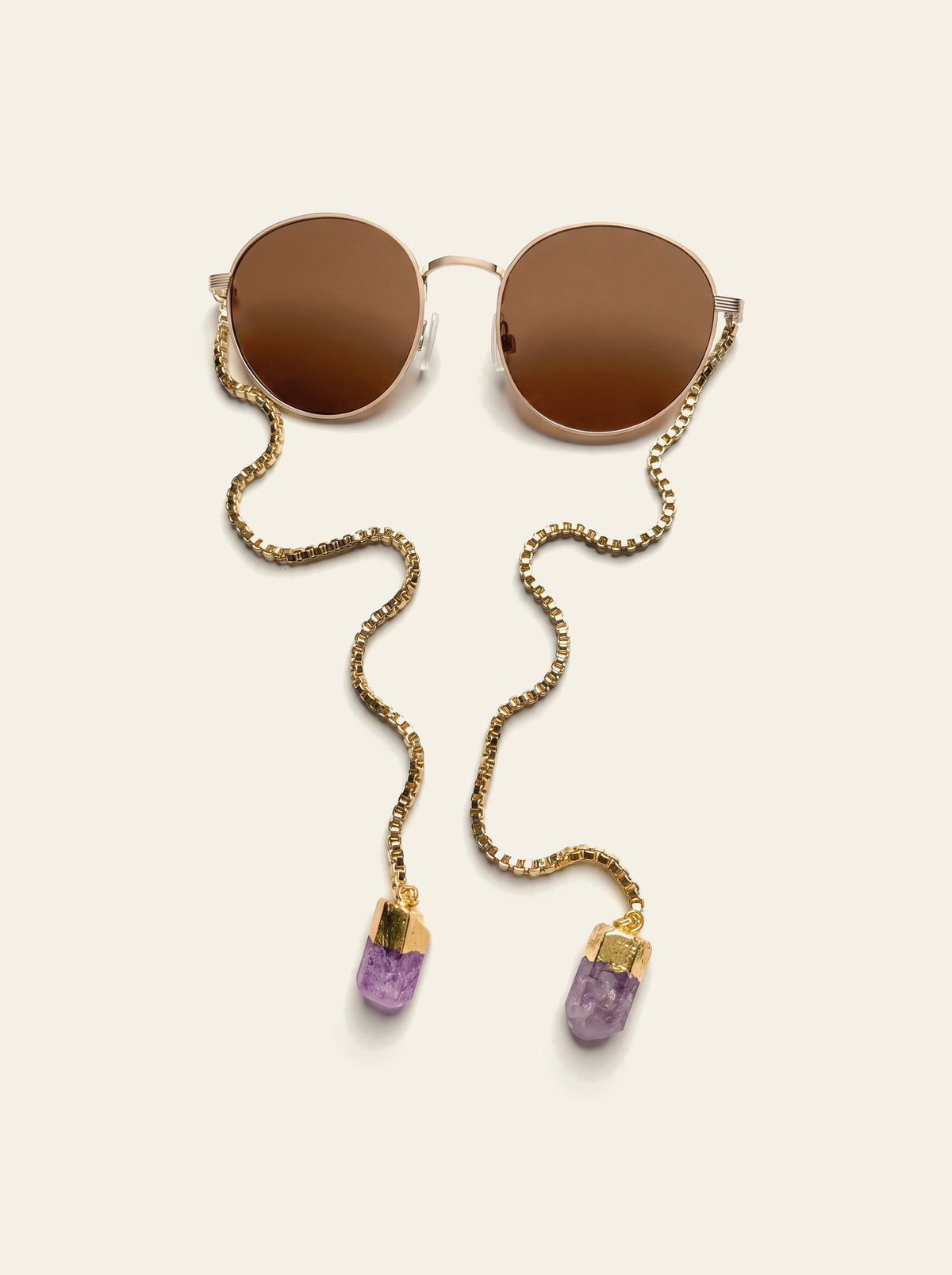 The Procida - top view of round gold frame with brown lenses, the temple-less gold chain draping down to two purple quartz stones in gold caps
