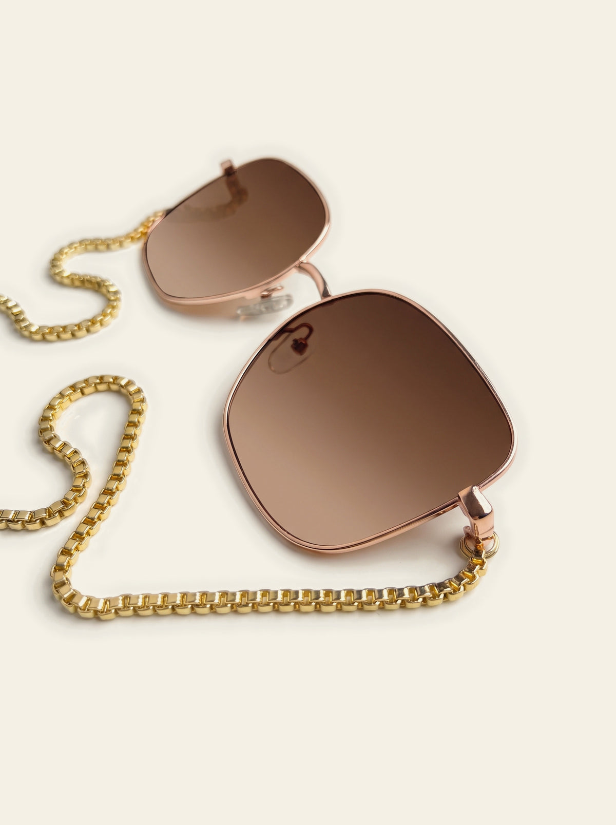 The Menton - close-up of the square gold-finished frame and brown gradient lenses with the chain draped below