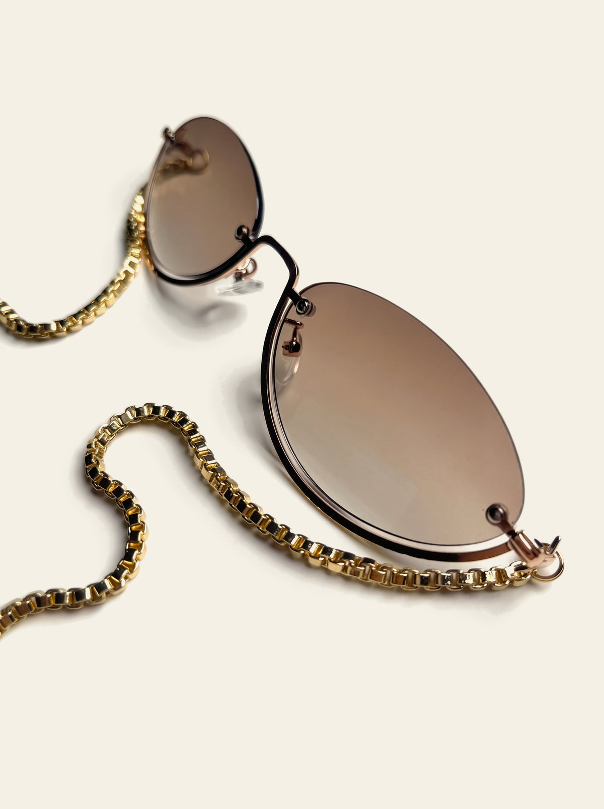 The Rapallo - front view of rimless oval brown gradient lenses with the gold chain draped down to two blue quartz stones