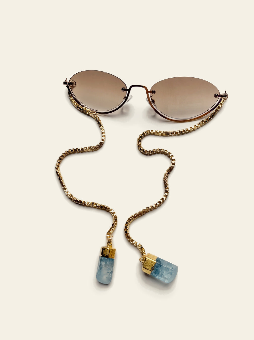 The Rapallo - top view close-up of a rimless brown gradient oval lens on a fine gold wire with the gold box chain beside it