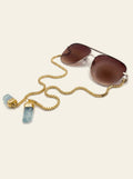 The Camogli - gold semi-rimless aviator sunglasses with brown gradient lenses, seen from three-quarter view, gold chain trailing to two raw blue quartz stones