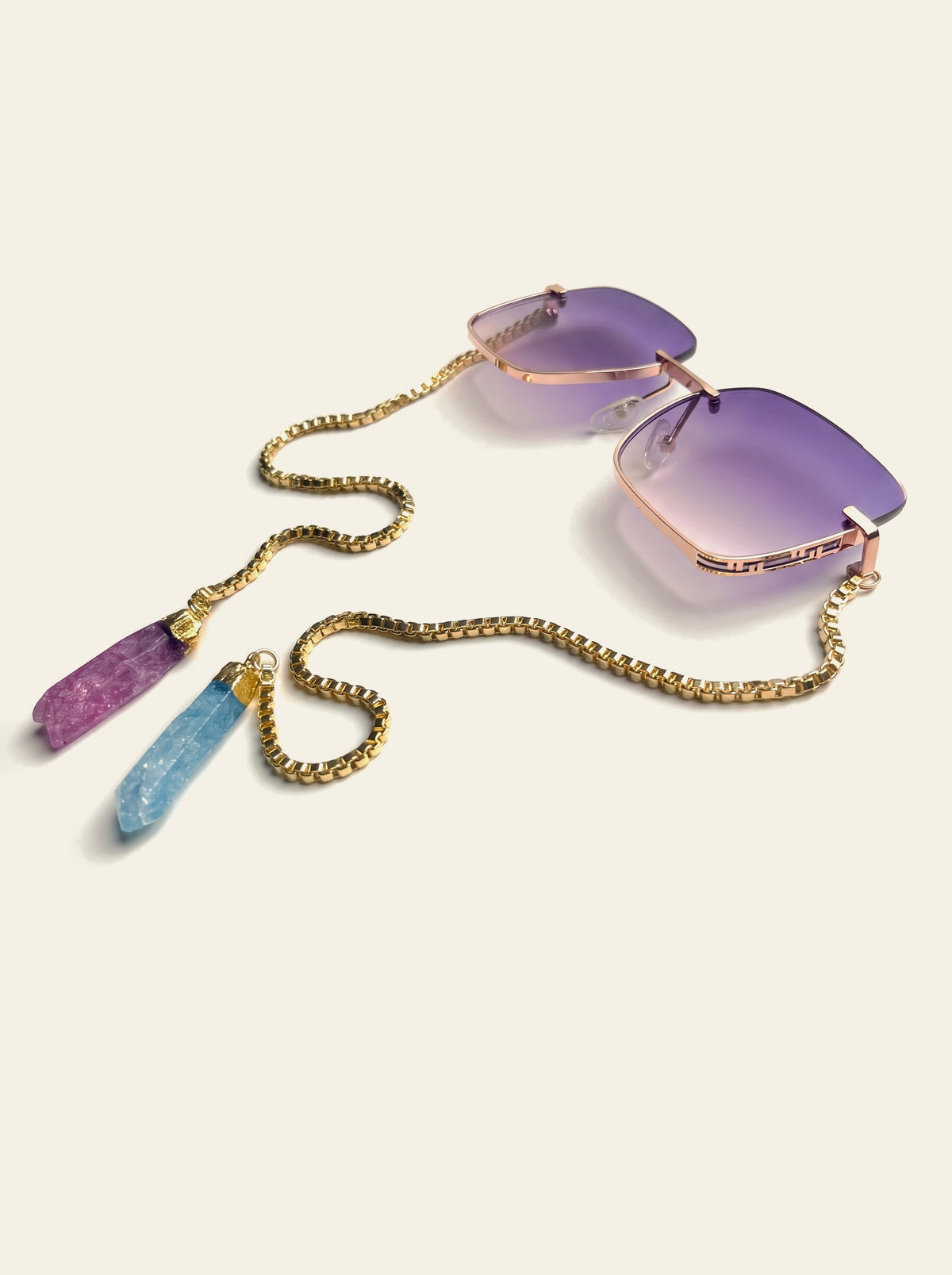 The Mykonos - rimless square sunglasses with purple gradient lenses, gold chain and raw pink and blue quartz stones, three-quarter view