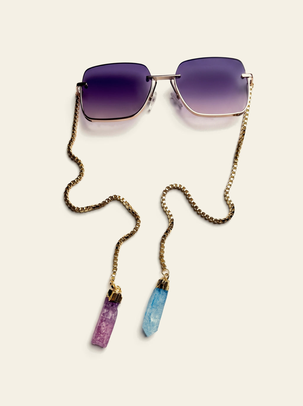 The Mykonos - rimless square sunglasses with purple gradient lenses and gold chain seen from above, pink and blue quartz stones below