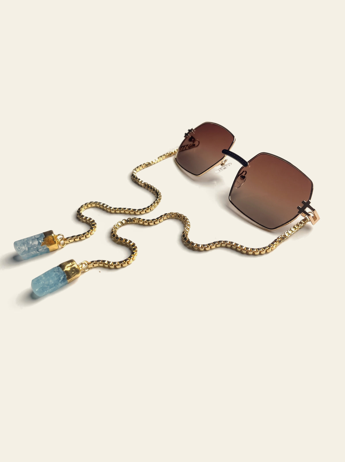 The Santorini - rimless square sunglasses with brown gradient lenses, gold box chain and two raw blue quartz stones, three-quarter view