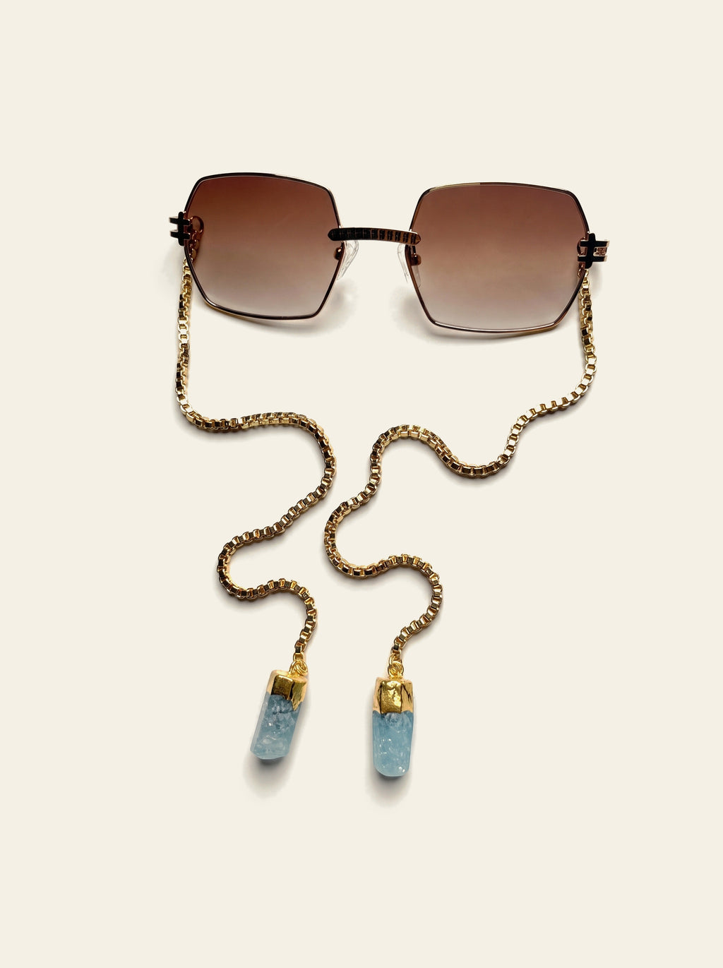The Santorini - rimless square brown gradient sunglasses seen from above with gold chain and blue quartz stones