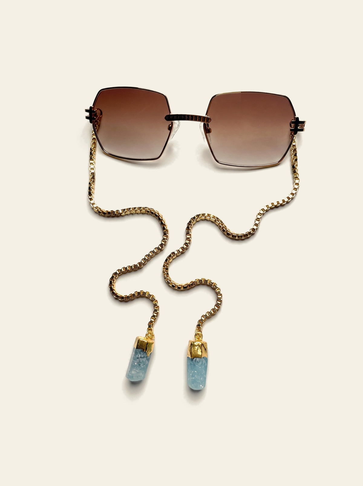 The Santorini - rimless square brown gradient sunglasses seen from above with gold chain and blue quartz stones