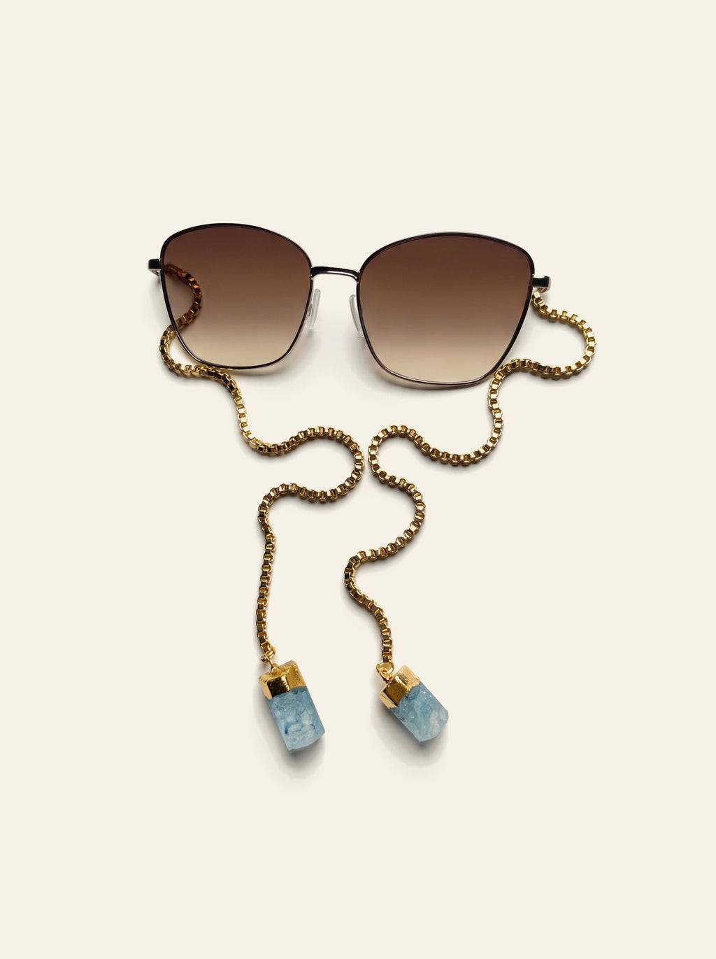 The Biarritz - close view of the gold butterfly frame and brown gradient lenses with the gold box chain draped alongside