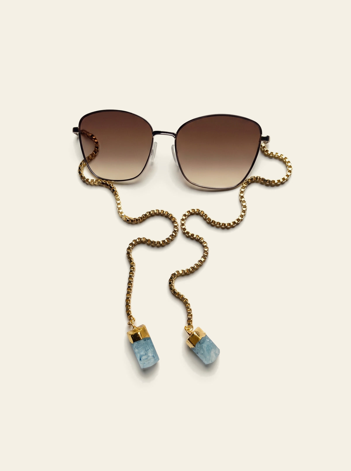 The Biarritz - close view of the gold butterfly frame and brown gradient lenses with the gold box chain draped alongside
