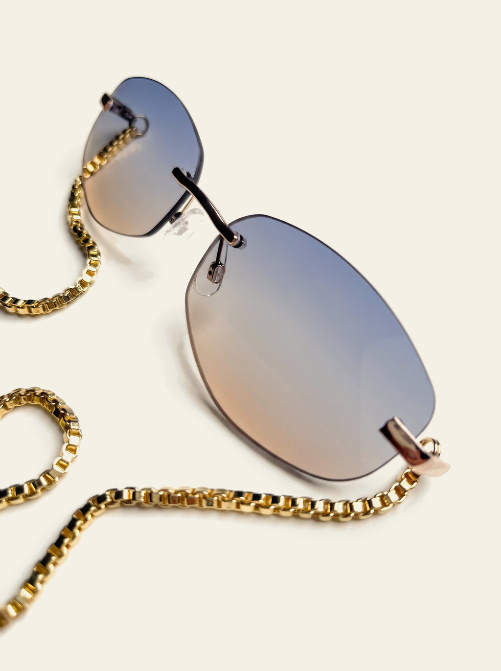 The Stresa - close-up of a rimless blue-grey gradient lens fading to a warm rose haze, with gold end-piece and box chain