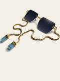 The Sardinia - rimless square gold sunglasses with deep ink-blue lenses, three-quarter view, gold chain and two pale blue quartz stones