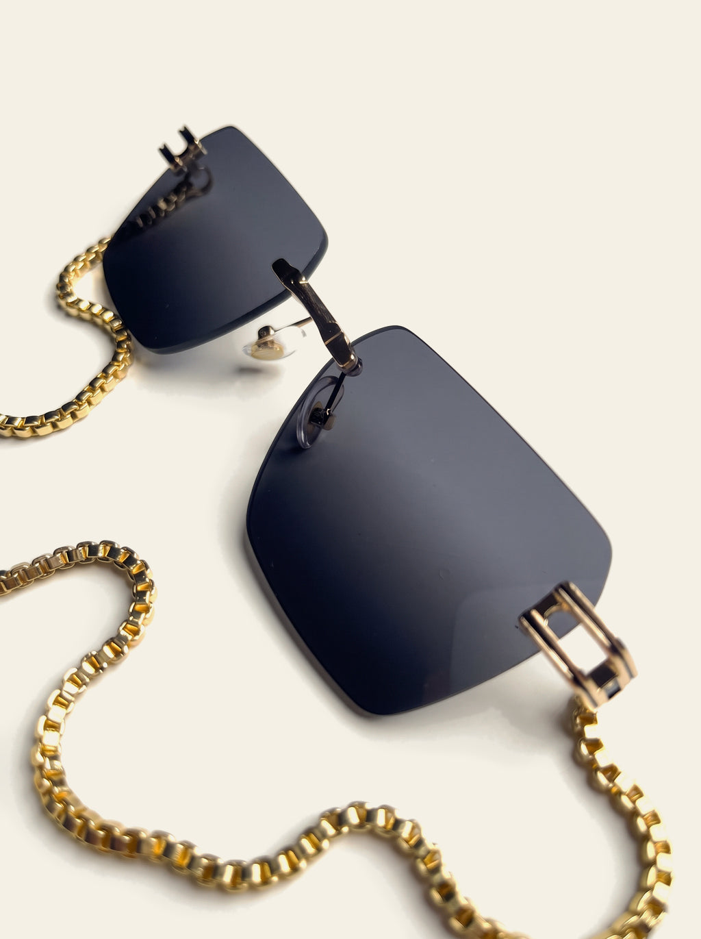 The Sardinia - front view of rimless square dark blue lenses on a slim gold bridge with chain draped below