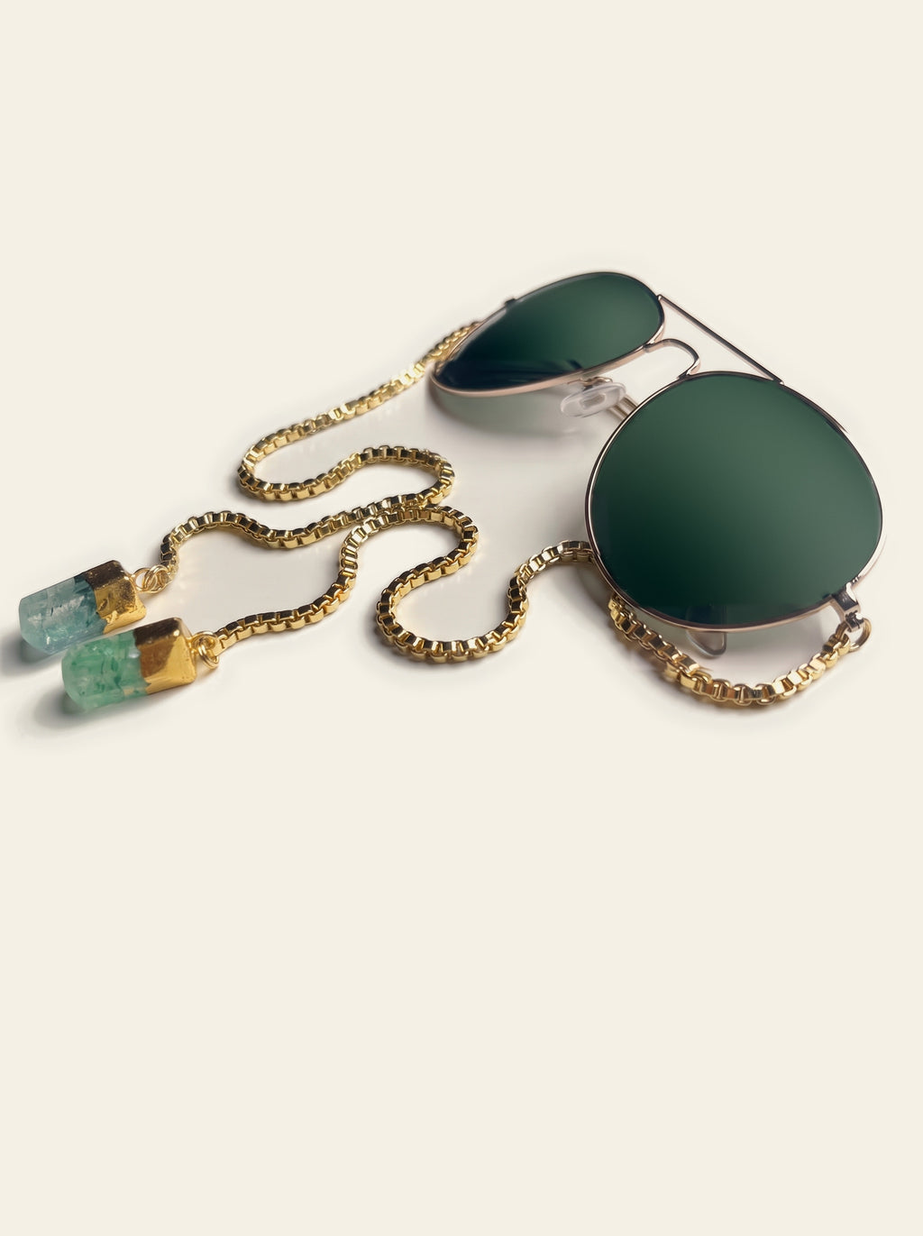 The Saint-Tropez - three-quarter view of gold aviator sunglasses with dark green lenses and a gold box chain ending in two raw mint green quartz stones